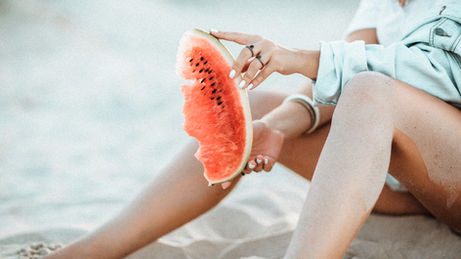 A woman on the beach eating watermelon, which promotes dental health.