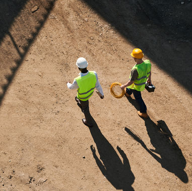 Aerial view of two construction workers in hard hats and safety vests walking outdoors on a construction site.