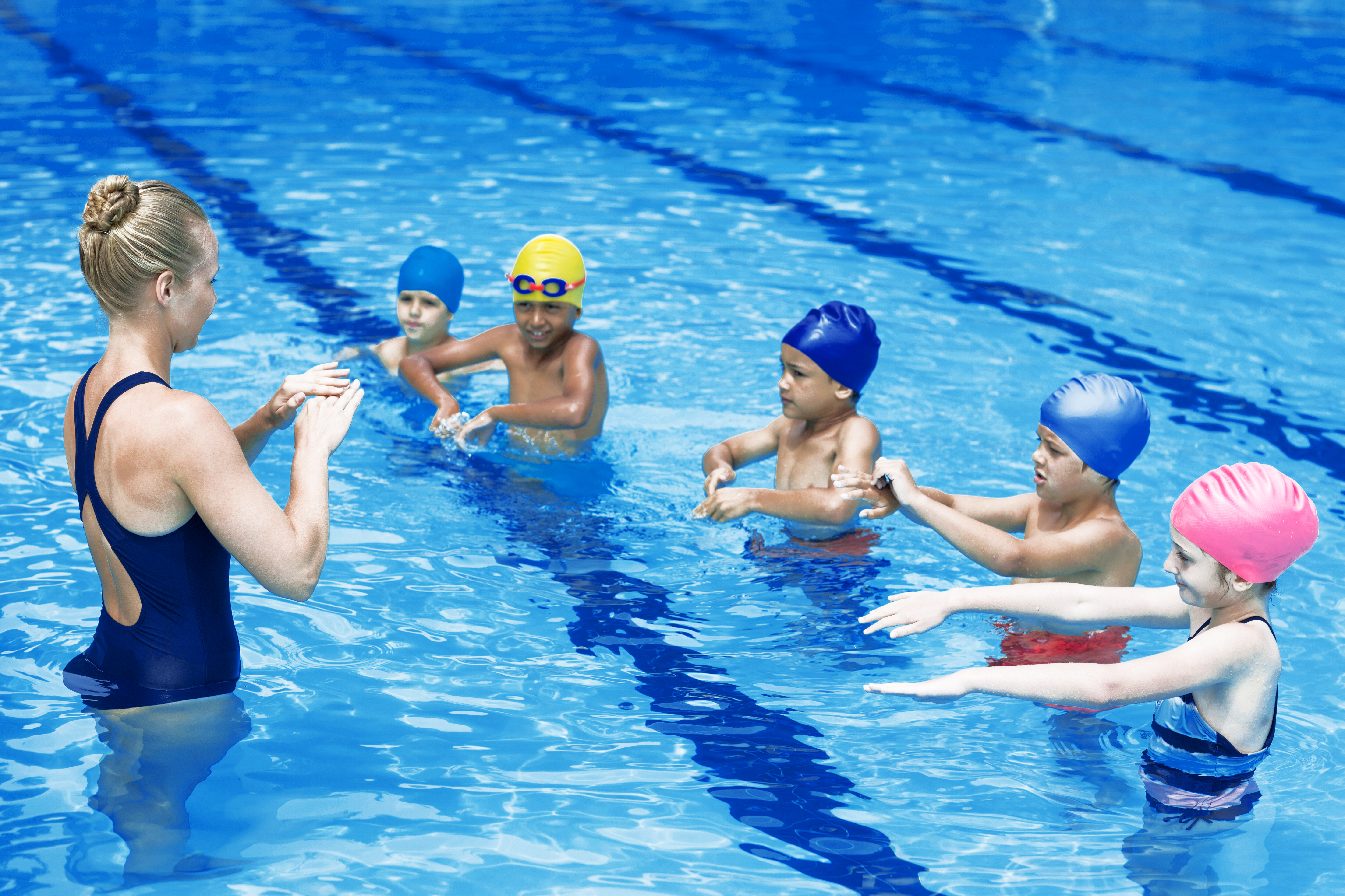 Eine Schwimmlehrerin mit einer Gruppe Kindern, die gemeinsam eine Übung im Wasser machen.