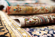 Close-up of intricately patterned, colorful Persian rugs, partially rolled