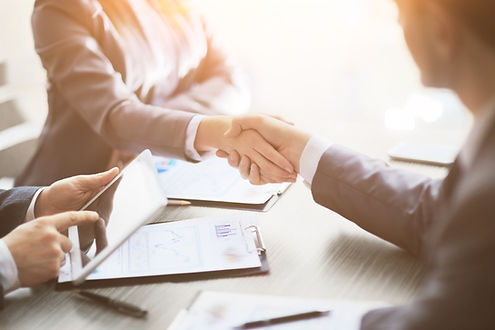 Two people in business attire shaking hands at a desk