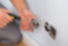 Close-up of electrician hands with screwdriver installing wall socket on a white wall