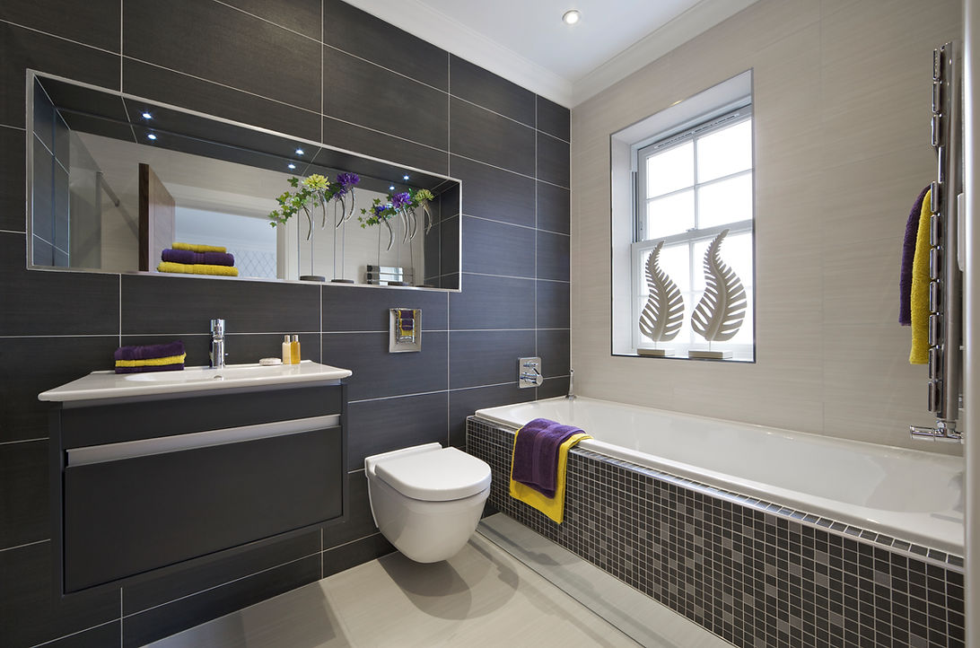 A modern bathroom featuring a bathtub with decorative towels, a sleek vanity with a sink, and a large mirror above the sink. The walls are tiled in dark colors, and there are plants displayed decoratively on the mirror ledge