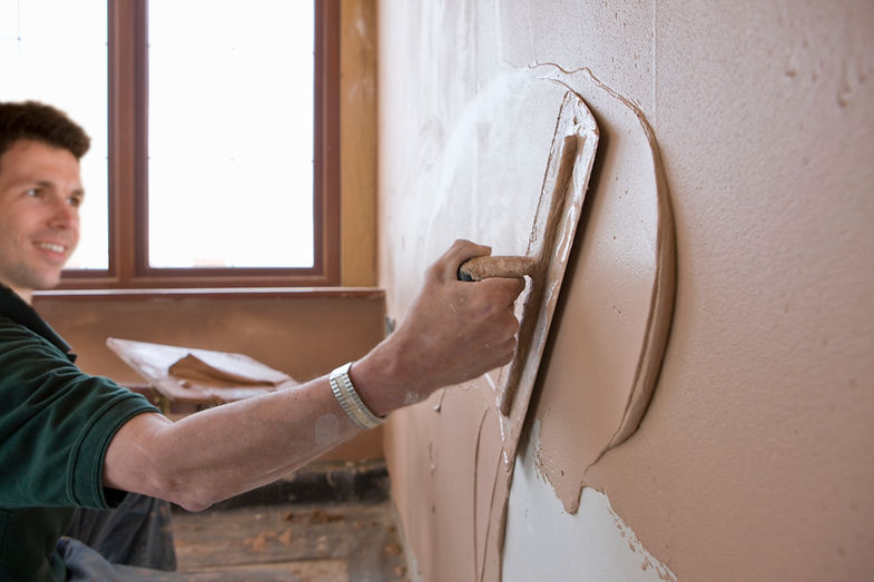 Male plasterer plastering wall with trowel