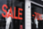 Retail storefront window displaying large red 'SALE' text and '-70%' discount signs with white mannequins, indicating a liquidation or closing sale