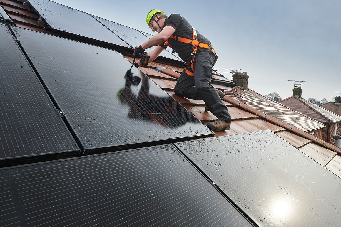 A worker in safety gear installs solar panels on a sloped rooftop under a clear sky