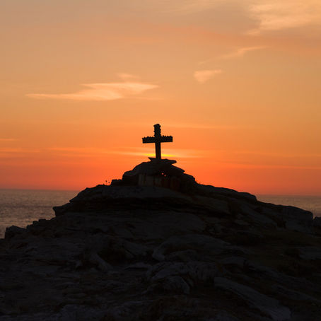 A cross on top of a hill at dawn.