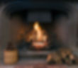 A roaring fire within a large stone arched fireplace, with pile of logs and basket of pine