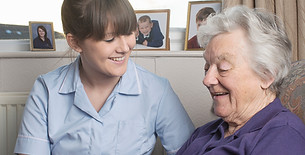 Female caregiver in uniform smiling and looking down at a happily laughing elderly woman