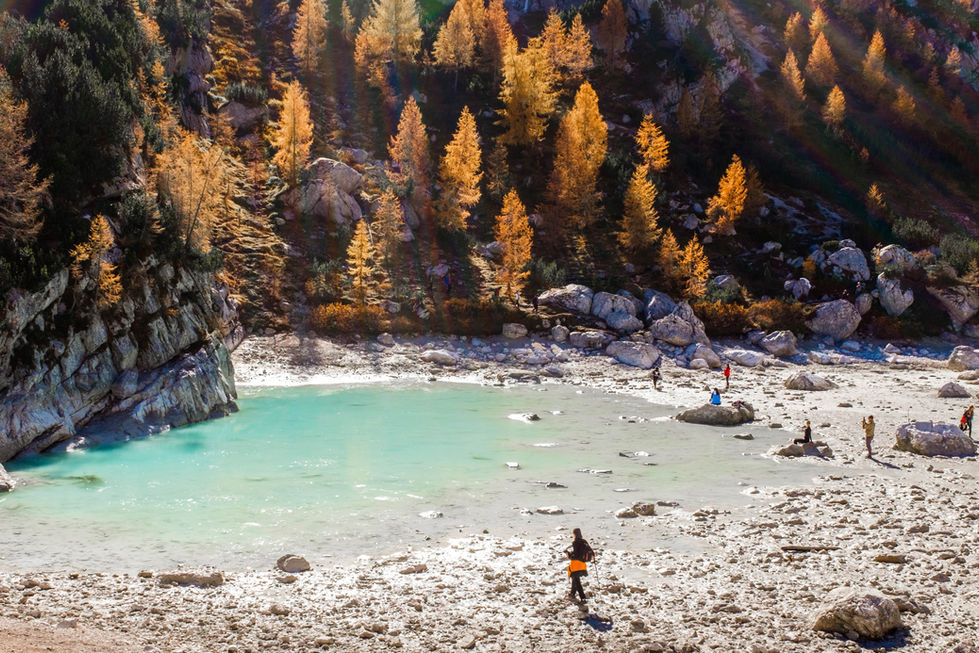 People enjoying a beautiful turquoise lake in the mountains, with golden leaves on the trees.