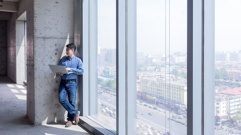 Man works on laptop standing in an empty office with large windows