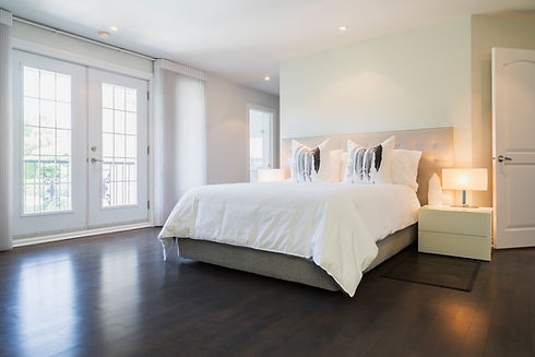 Master bedroom with bed, white lacquered nightstands and dark wooden flooring