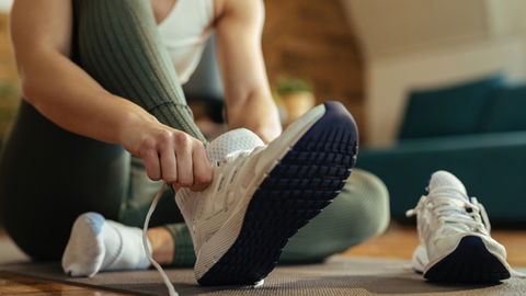 Personne assise sur un tapis, nouant une chaussure de sport blanche; ambiance calme dans un salon lumineux.