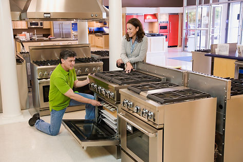 A man kneels inspecting an open oven in an appliance showroom