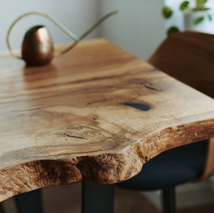 Rustic wooden table with live edge, a copper watering can, and plant in the background. Natural textures create a cozy, earthy feel.