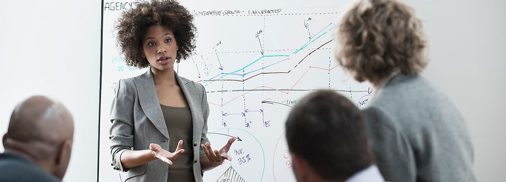Black professional woman leading meeting with whiteboard and a white woman and man listening intently
