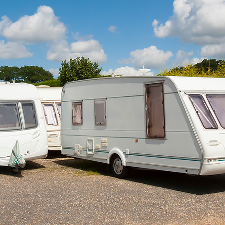 Three white caravans parked on a gravel lot under a bright blue sky with fluffy clouds