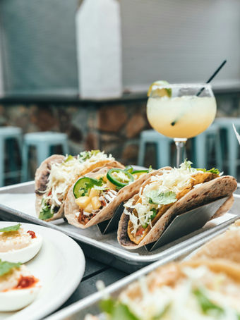 Three tacos on a tray with a margarita and deviled eggs