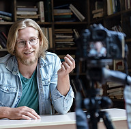 Homem gravando gravando na sua biblioteca com uma câmera para seu canal de youtube