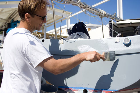 A marine specialist inspecting and working on the hull of a white boat at a boatyard