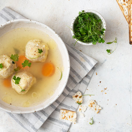 A comforting matzo ball soup inspired by Tampa Bay’s Jewish community, featuring fluffy dumplings, sweet carrots, fresh cilantro, and matzo crackers on the side—South Tampa tradition with a local twist.