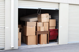 Open roll up door of a white self storage unit filled with cardboard boxes and furniture in a warehouse building