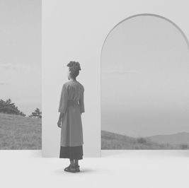 A woman stands with her back to the viewer, facing an arched doorway that opens onto a misty landscape — evoking the threshold between two worlds, reflecting the emotional limbo of a late autism diagnosis.