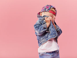 Child hiding behind their jacket in front of a pink background