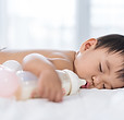 A baby boy sleeping beside a milk bottle