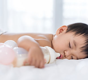 A baby boy sleeping beside a milk bottle
