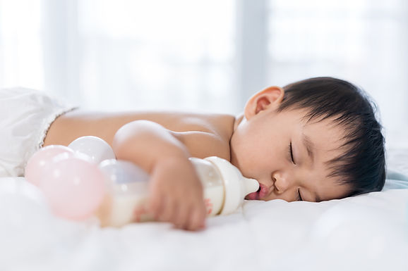 Un petit garçon dormant à côté d’un biberon de lait