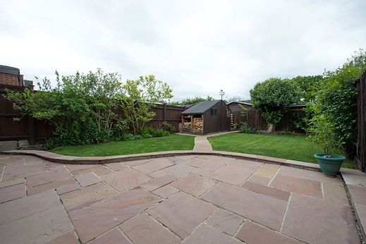 Spacious natural stone patio area overlooking a garden lawn and wooden shed