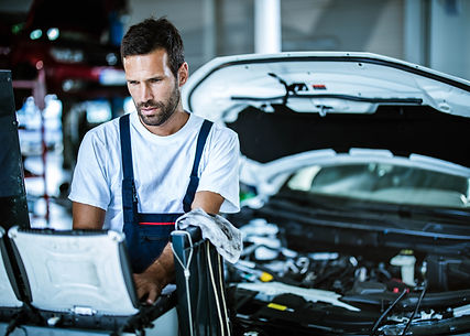 Auto repairman using laptop while working on car diagnostics in a workshop