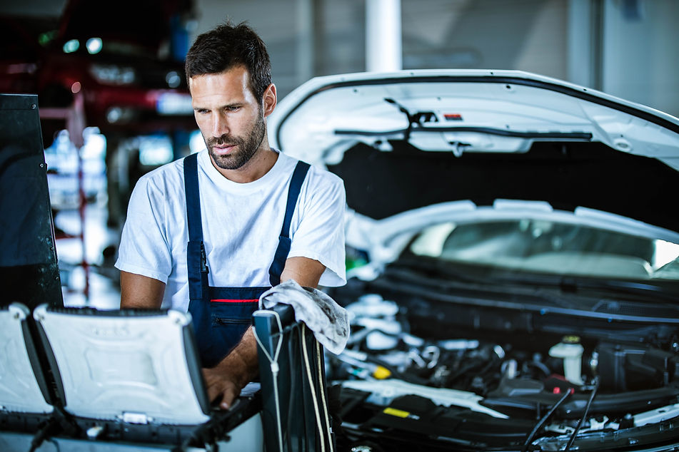 Auto repairman using laptop while working on car diagnostics in a workshop