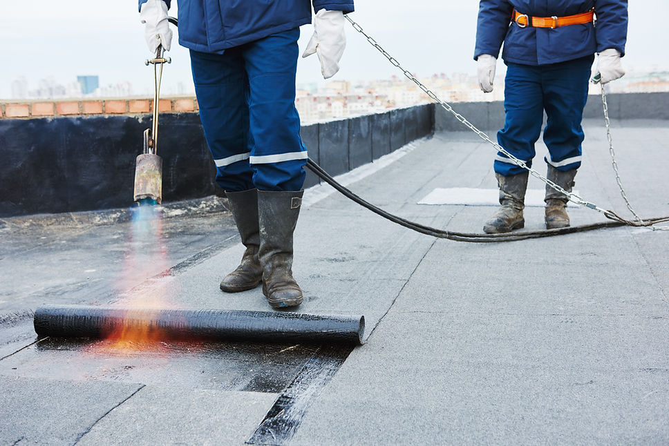 A worker torching down a roll of bituminous roofing material