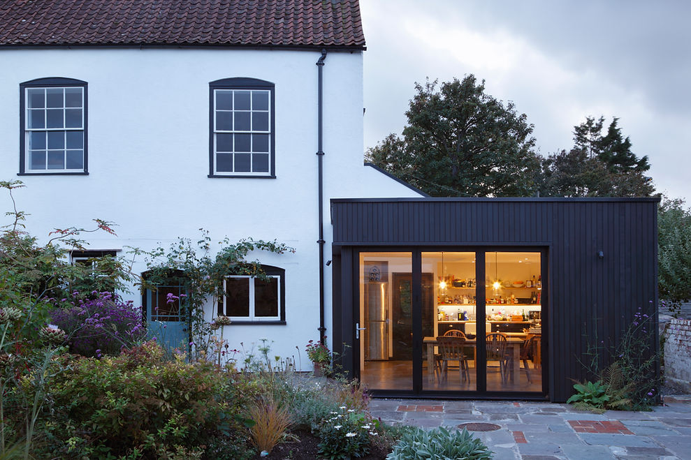 A historic white house with a modern black extension glows warmly at dusk