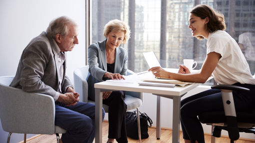 Older couple sitting at a table with a financial advisor, reviewing documents and smiling, discussing retirement planning.