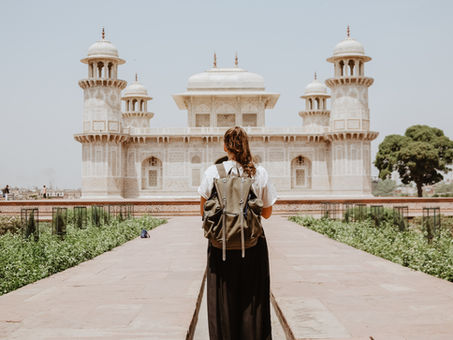 A young woman with a backpack on standing back from an old Indian temple and looking at it. A narrator in a story can look at events in the past from some distance away.