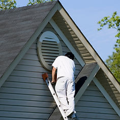 A tradesperson on a ladder painting the upper exterior of a house