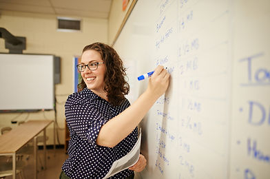 A teacher instructs her class as she writes on the whiteboard during her engaging lesson.