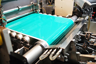 A bright turquoise sheet is processed through an industrial machine with rollers