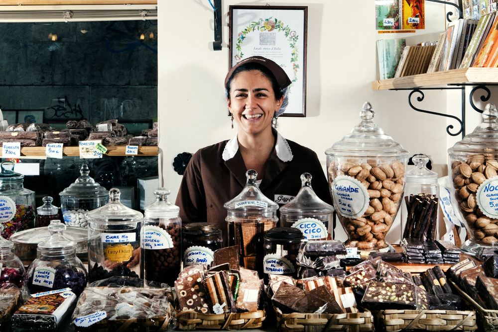 Baker in shop standing in front of counter containing jars of baked goods