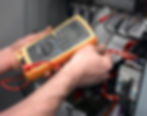 A technician uses a digital multimeter with red and black leads to test electrical connections