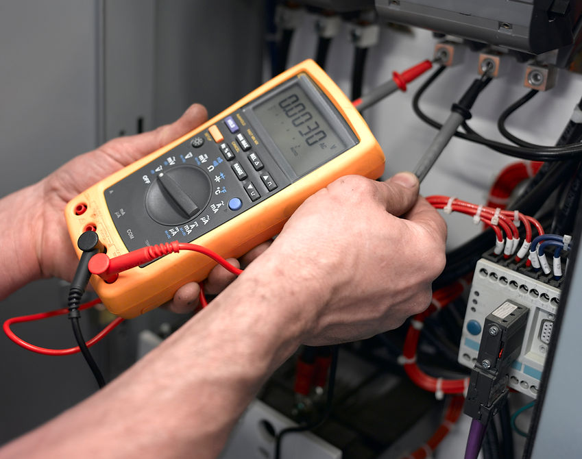 Electrician holding digital multimeter probes to diagnose potential faults
