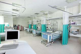 Empty hospital beds with teal privacy curtains in a surgical center recovery room