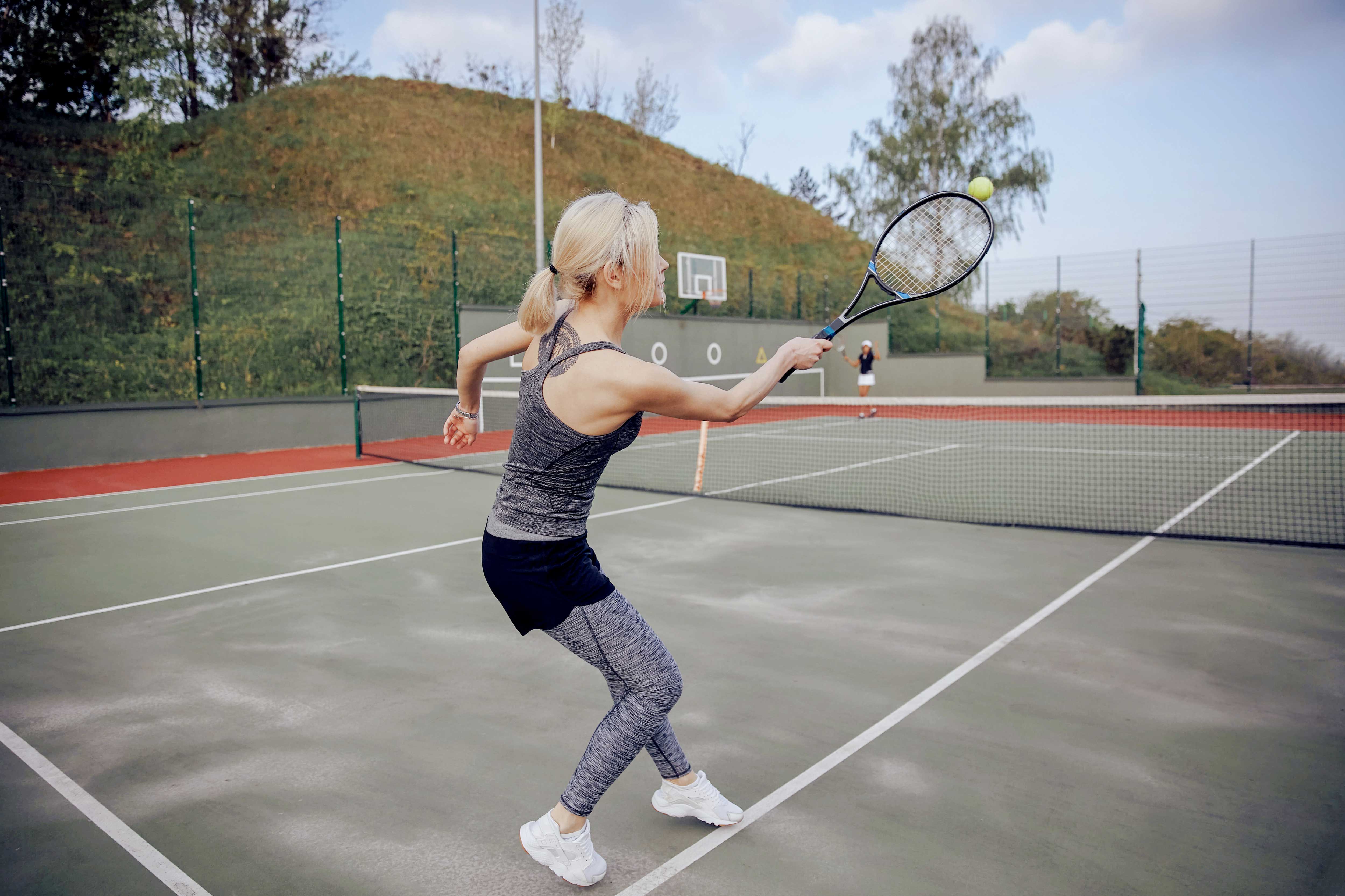 A woman playing tennis on an outdoor court, hitting a ball with her racket.