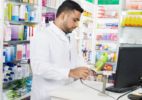 Apotheker scannt Produkt an Kasse in Verkaufsbereich mit Medikamenten und Verkaufsregalen
