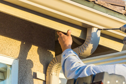 A man attaching aluminum rain gutter and downspout to fascia of house