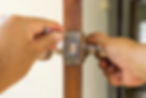 A person using a screwdriver to adjust a door lock on a wooden door