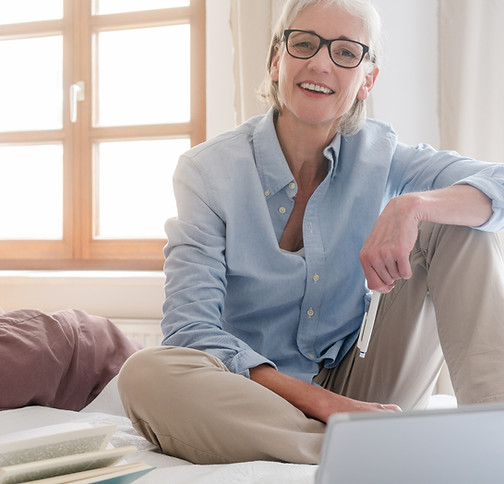 Mujer de tercera edad en la cama con un ordenador y feliz por poder solucionar su problema de salud por vía telemática
